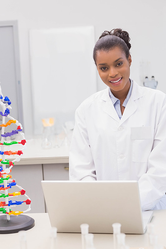 非裔美国女性科学家在实验台上使用笔记本电脑,旁边有DNA模型和试管图片下载